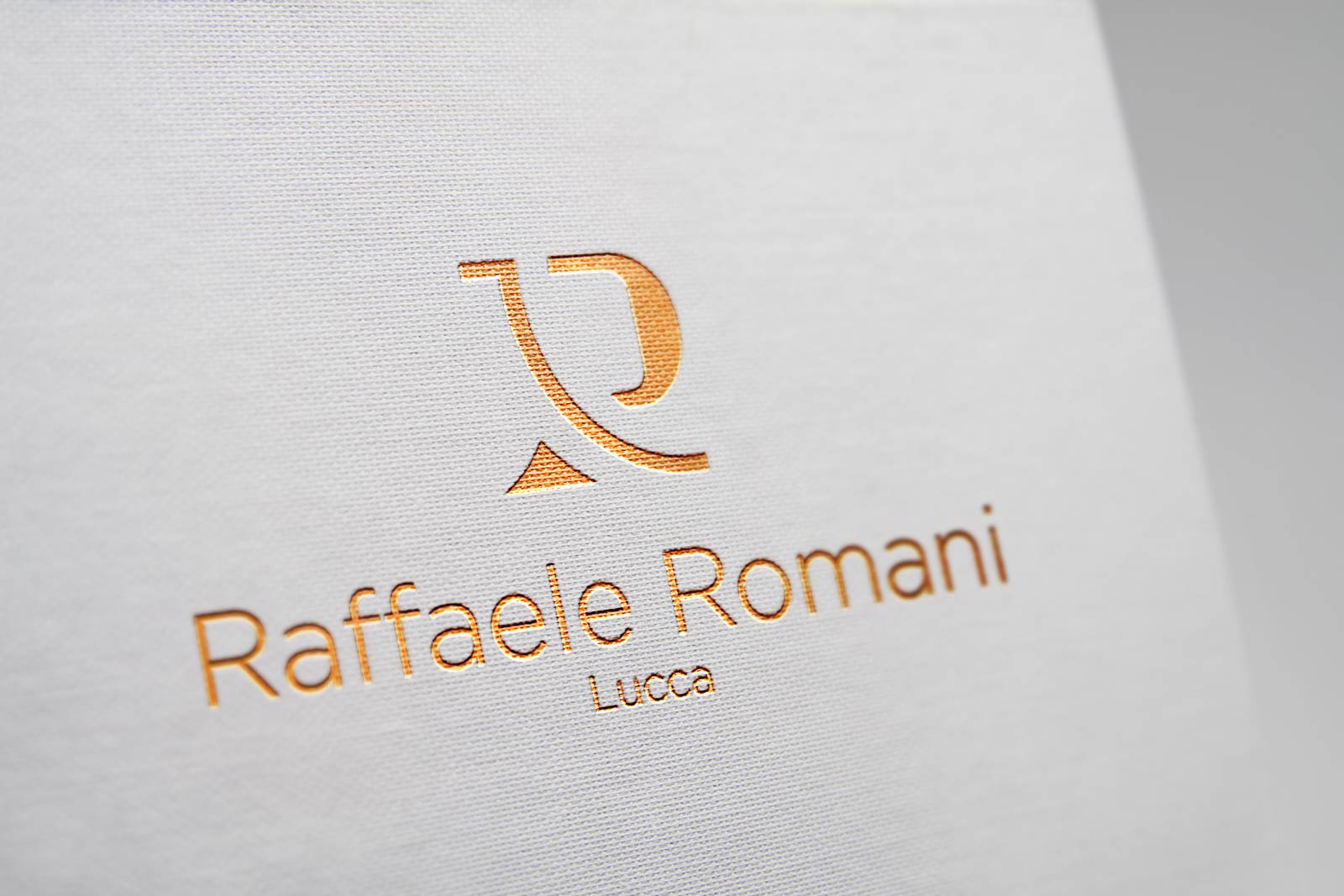 Logo e brand identity di Raffaele Romani realizzato da SEBA! grafico di Gravellona Toce nel VCO del logo dorato su foglio bianco